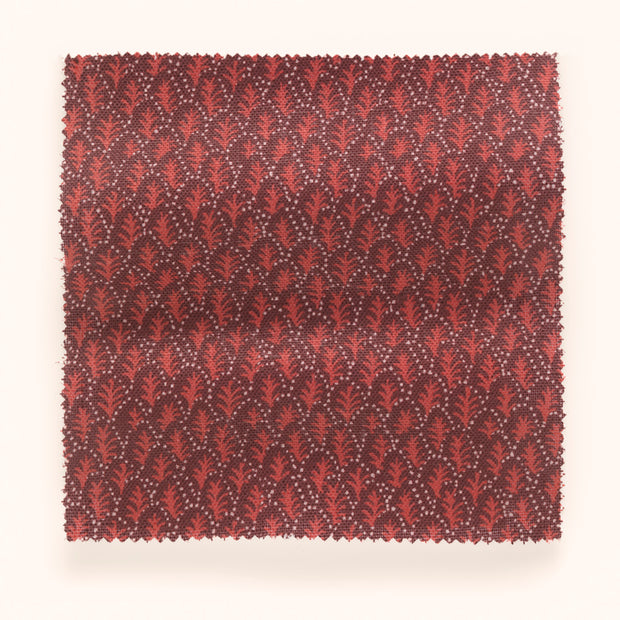 A yard of fabric with a red and pink microprint design featuring tree patterns.