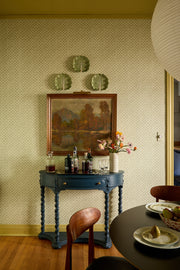Vintage interior with a blue table, chairs, and decorative items against a patterned wall. Citron - Madras Geo Wallpaper by Panel
