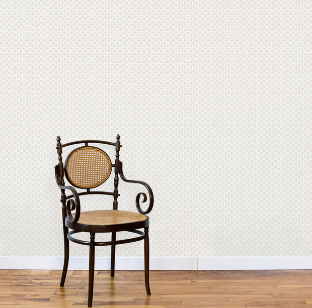 Vintage chair with a woven seat against a light patterned wallpaper. Shale - Madras Geo Wallpaper by Panel