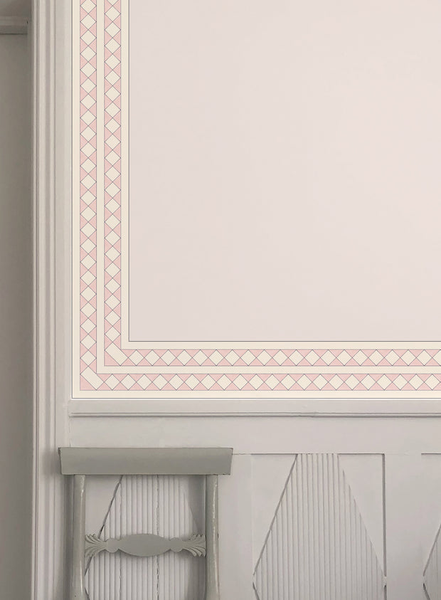 A pink wallpaper border with a geometric pattern installed on a wall, showing a traditional design with floral elements - Pink - WP Harlequin Wallpaper Border, Non Woven, 10m Roll