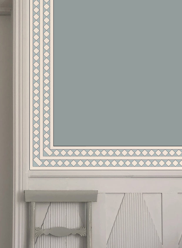 A strip of light blue wallpaper with a geometric pattern, Harlequin trim, placed on a wall with visible wooden trim and a gray background.