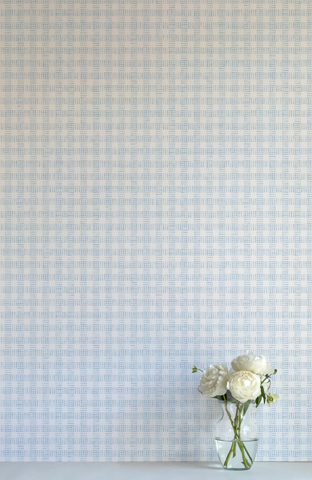 A wall adorned with blue and white checkered wallpaper, featuring a vase with white flowers in the foreground.