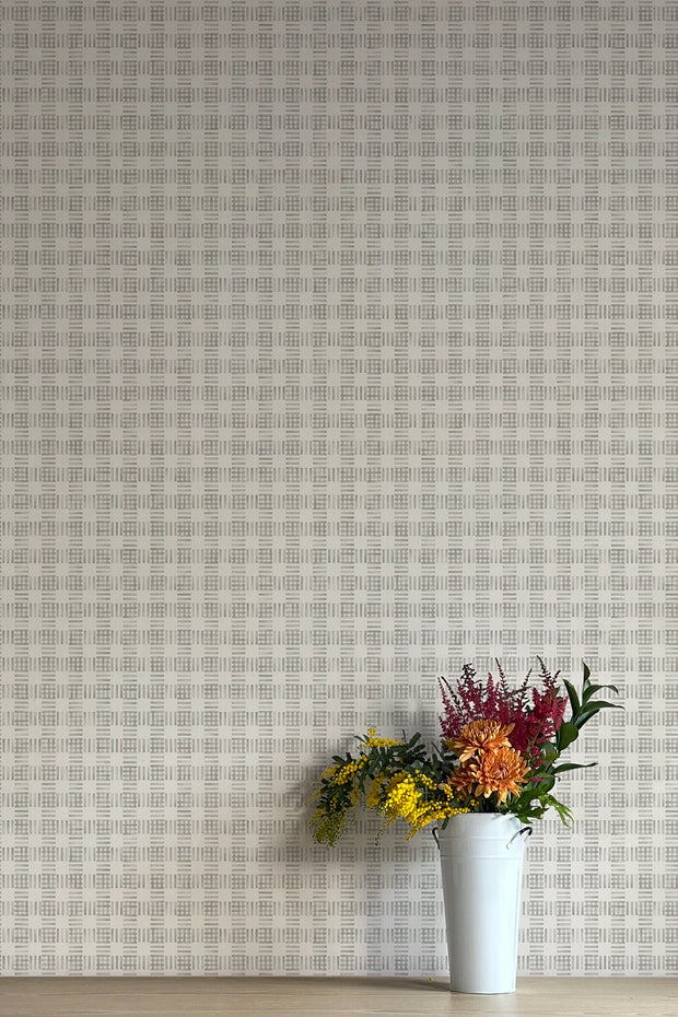 A wall adorned with a checkered patterned wallpaper, featuring a vase with colorful flowers on a table against this background.