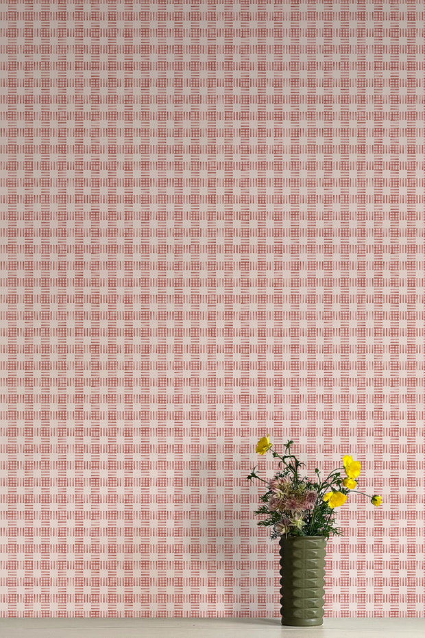 A vase with flowers placed against a pink checkered wallpaper background.