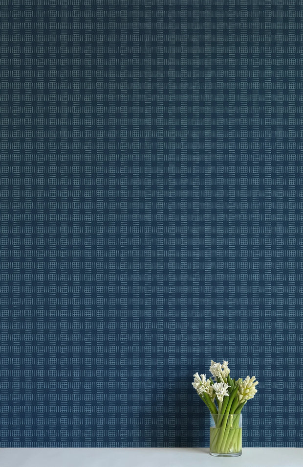 A section of navy blue wallpaper with a checkered pattern, trimmed to show a 27-inch width, displayed on a wall behind a vase with white flowers.