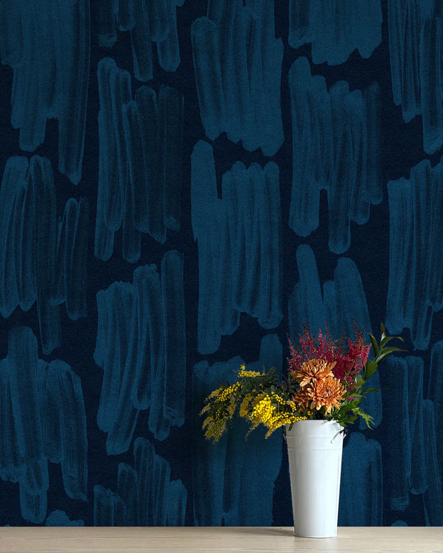 A section of blue wallpaper with a contemporary geometric pattern, displayed on a wall above a white vase with colorful flowers.