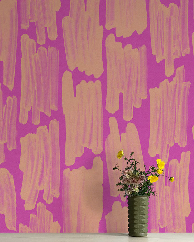 A wall adorned with a pink and purple abstract geometric patterned wallpaper, featuring a vase with flowers in the foreground.