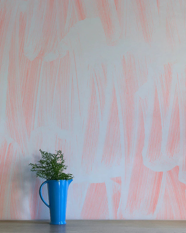 A section of wallpaper with abstract geometric patterns in pink and gray tones, next to a blue mug with a plant.