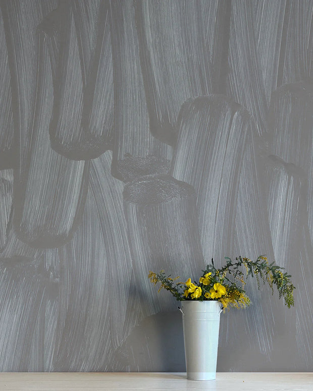 A section of wallpaper with a contemporary abstract design in gray, with a vase of flowers in front.