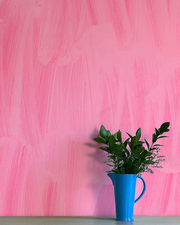 A section of pink wallpaper with a contemporary graphic design, featuring a blue vase with green leaves on a table.