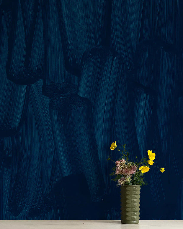 A section of blue wallpaper with a modern geometric pattern, featuring swirls and lines, displayed on a wall behind a vase with flowers.