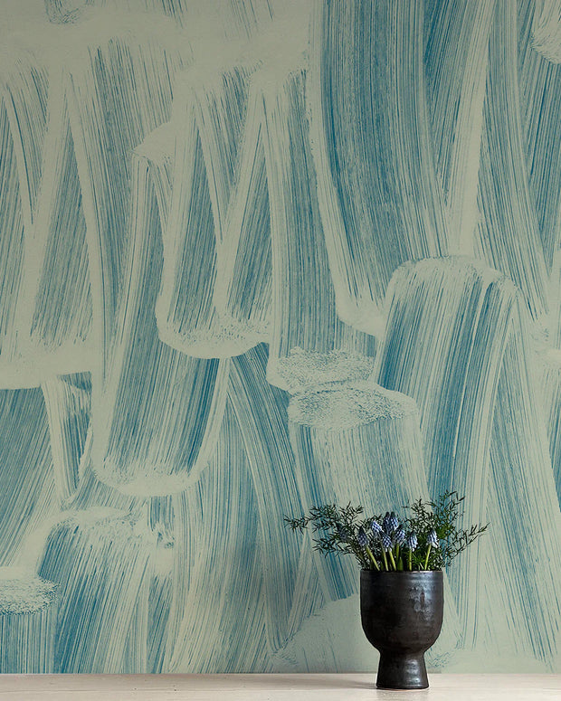 A section of wallpaper with a blue abstract pattern, trimmed to showcase the design detail, with a vase of flowers in the foreground.