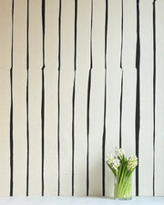 A wall adorned with black and beige striped wallpaper, featuring a vase with white flowers on a table in the foreground.