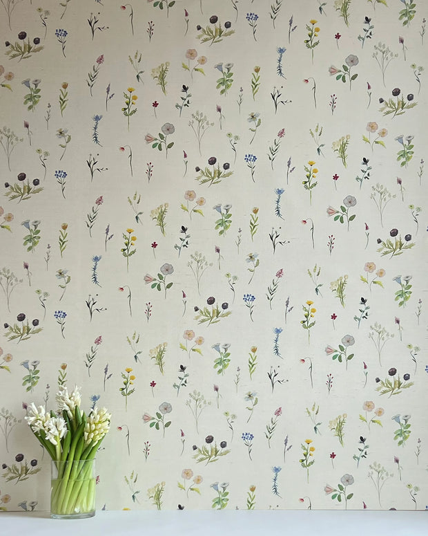 A wallpaper with a floral pattern featuring various flowers in different shades of beige, blue, green, pink, and purple, displayed on a wall.