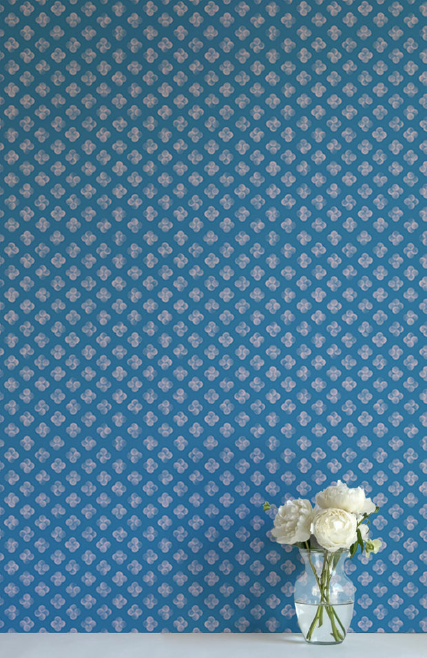 A wall adorned with blue wallpaper featuring a geometric dot pattern, in a room with a vase containing white flowers on a table - Quattro Alex’s Blue Wallpaper – Stylish Non-Woven Double Roll