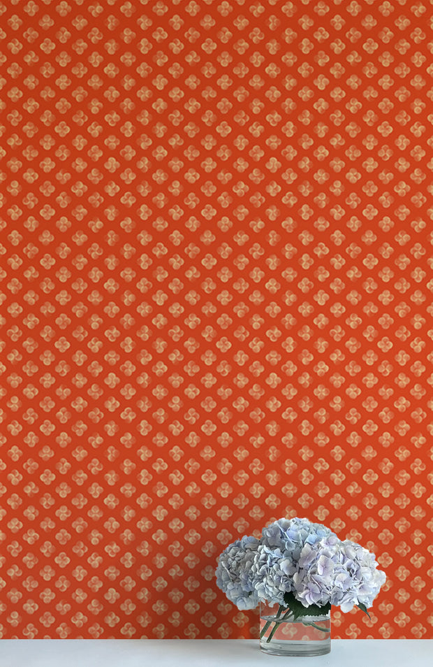 A roll of orange wallpaper with a geometric pattern of dots, placed on a wall behind a vase with purple flowers - Quattro Clementine Wallpaper – Modern Non-Woven Double Roll