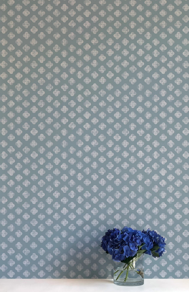 A section of wallpaper with a gray base and blue floral pattern, trimmed to a uniform width, displayed behind a vase with blue flowers - Quattro Sagaponack Gray Wallpaper – Contemporary Non-Woven Double Roll