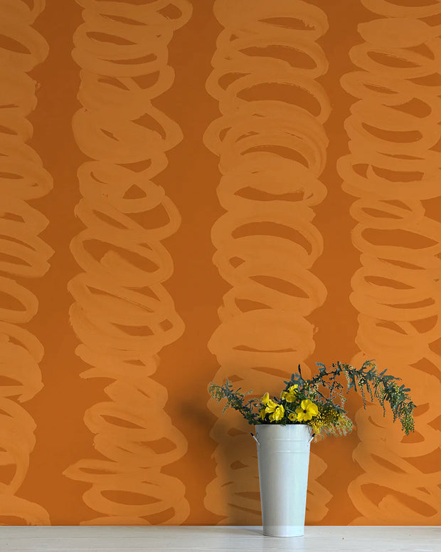 An orange wall adorned with a bold, curly, contemporary-style wallpaper. A white vase with yellow flowers is placed against this wall.