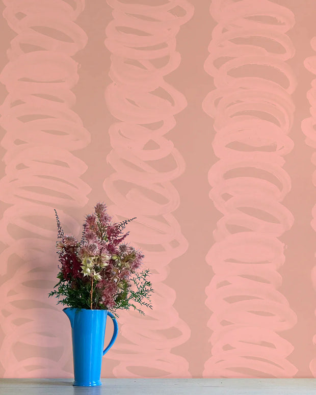 A wall adorned with pink wallpaper featuring a contemporary abstract design, and a blue vase with flowers placed against it.