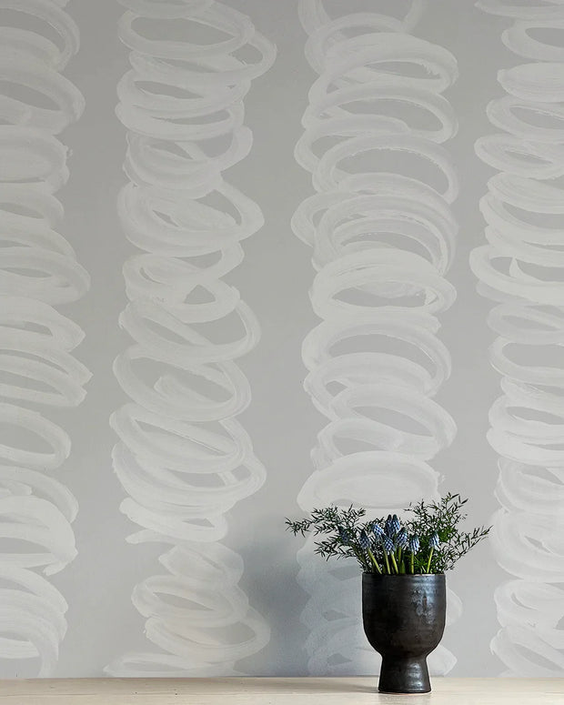 A section of wallpaper with a contemporary abstract design in gray and white, with a vase of flowers in the foreground.