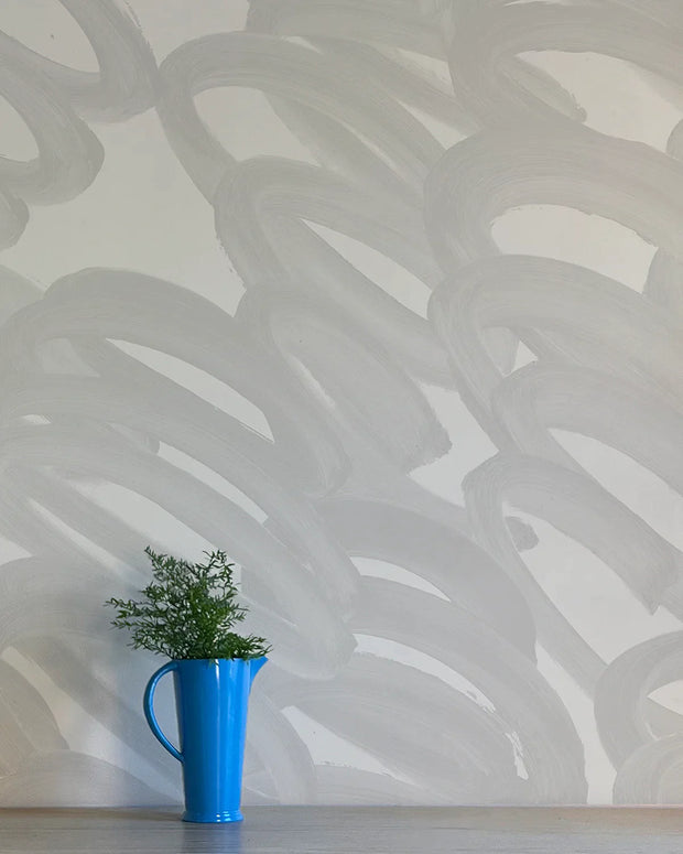 A section of wallpaper with abstract contemporary graphics in gray and white colors, with a blue mug and green plant on a white surface.