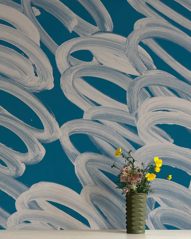 A section of wallpaper with abstract blue swirls and a vase with flowers placed against it.