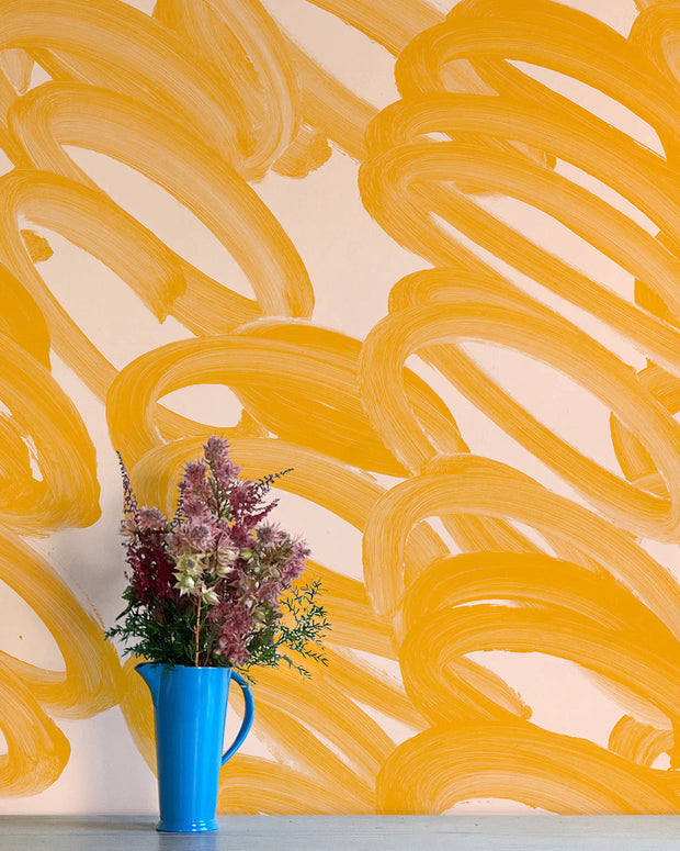 A section of wall adorned with yellow abstract wallpaper, featuring swirls and patterns, accompanied by a vase with pink and purple flowers.