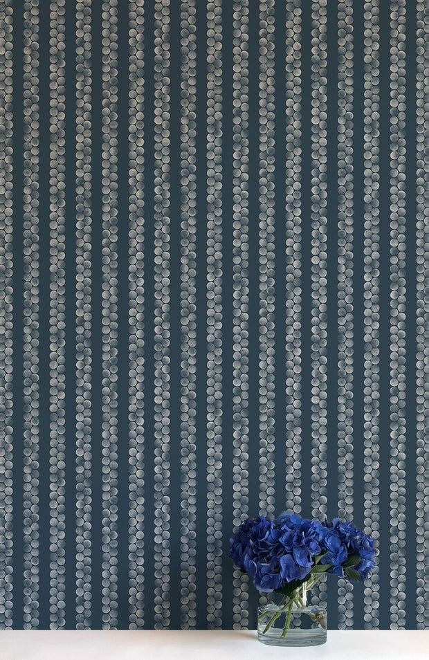 A wall adorned with blue and white striped wallpaper, featuring a vase with flowers in the foreground.