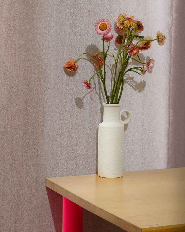 White vase with flowers on a wooden table against a textured wall. Sands Wallpaper – Flood Mural | Custom Type II PVC Free