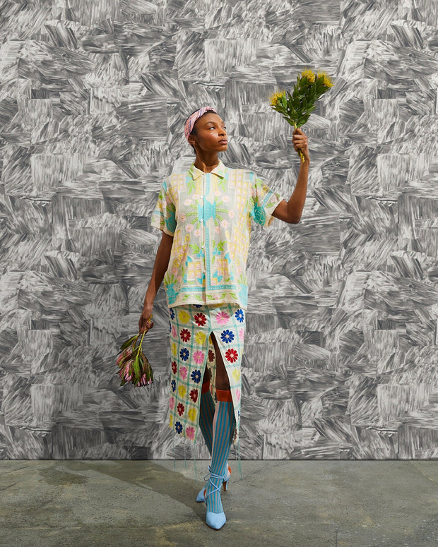 Person wearing a colorful outfit with floral patterns against a textured gray wall.