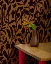 Vase with flowers on a table against a floral-patterned wall.