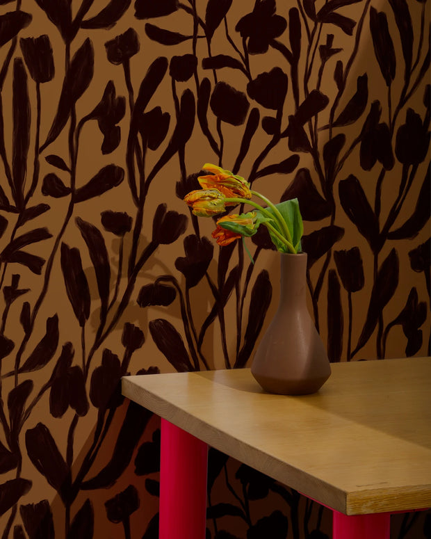 Vase with flowers on a table against a floral-patterned wall.