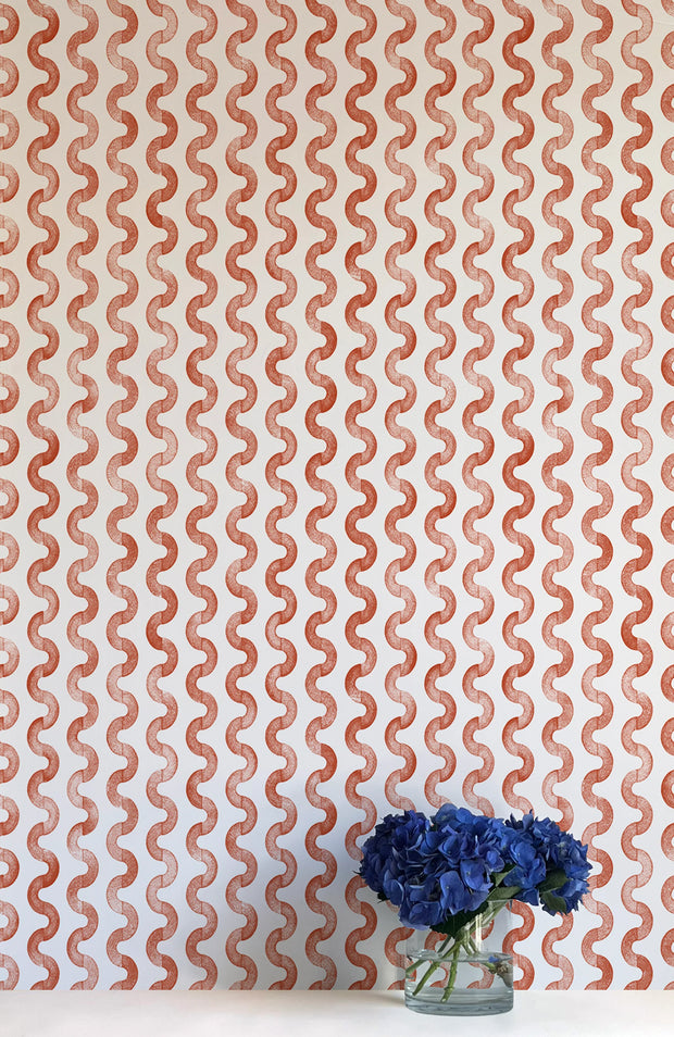 A wall adorned with orange and white striped wallpaper, featuring a vase with blue flowers on the surface.