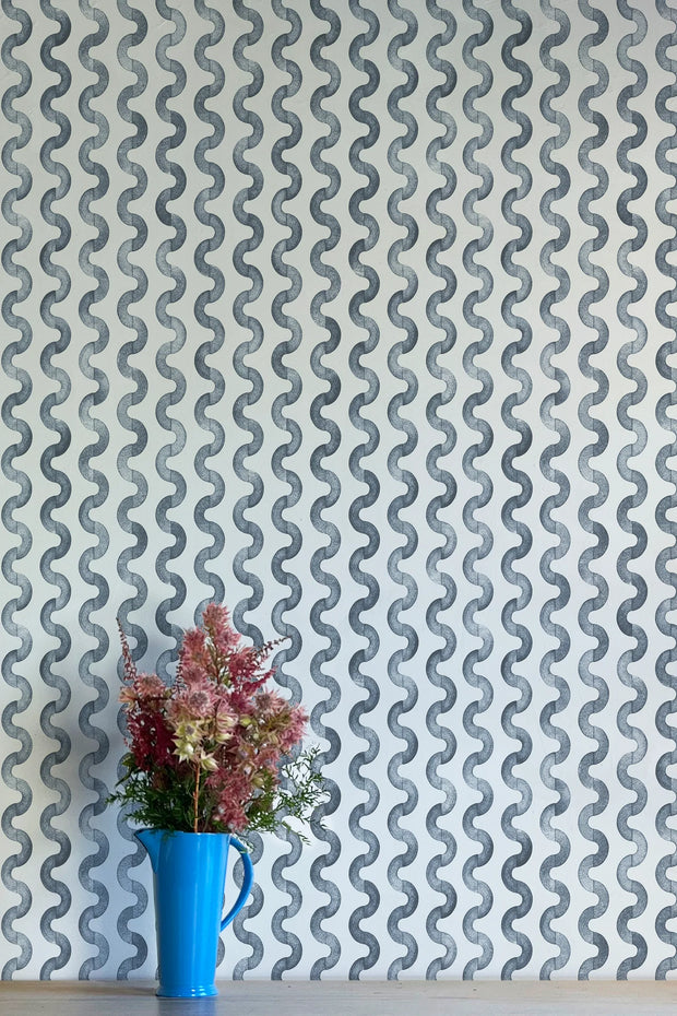 A wall adorned with blue and white geometric patterned wallpaper, featuring a vase with pink flowers to the bottom right.