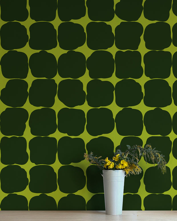 A wall adorned with green wallpaper featuring a geometric pattern of different shaped blocks.  Apple Wallpaper by Blot | Non Woven Double Roll, 27” Trimmed